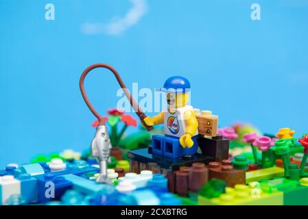 Florianopolis, Brasilien. 20. September 2020: Glücklicher Mann Minifigur in Tank-Top und Kappe auf einer Holzbank sitzen Angeln für einen Fisch. Angeln ist ein Sport p Stockfoto