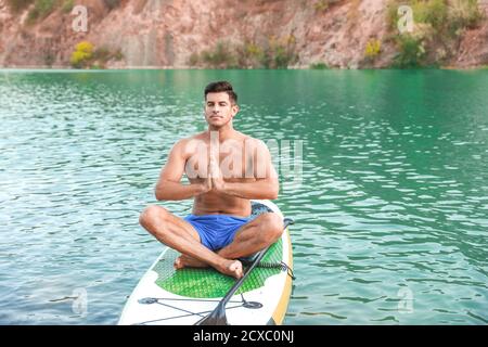 Junger Mann, der Yoga auf dem Paddelbrett im Fluss praktiziert Stockfoto