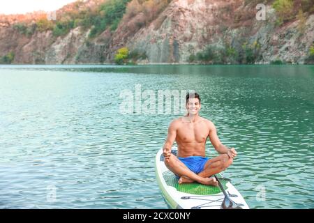 Junger Mann, der Yoga auf dem Paddelbrett im Fluss praktiziert Stockfoto