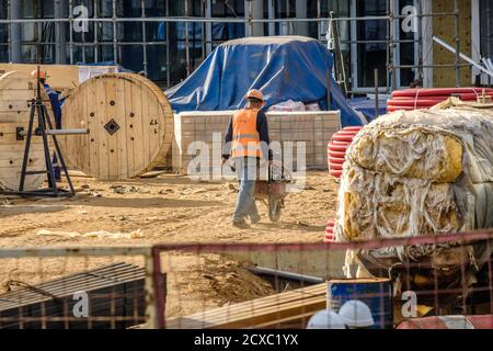 Moskau. Russland. 06. September 2020 EIN Baumeister in Uniform und ein Schutzhelm auf einer Baustelle transportiert Baustoffe in einem Trolley Stockfoto