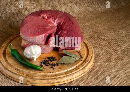 4 Pfund rohes Rindfleisch auf einem Holzbrett. Rohes Fleisch mit scharfer Paprika, Knoblauch, schwarzem Pfeffer und Lorbeerblättern auf einem Schneidebrett. Familienschlachter Sho Stockfoto