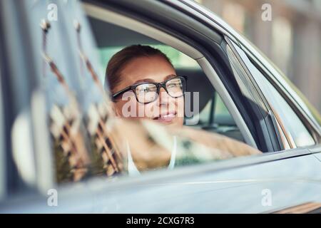 Geschäftsreise. Eine wunderschöne Geschäftsfrau mittleren Alters, die eine Brille trug und aus einem Autofenster schaute, während sie auf dem Rücksitz im Taxi saß Stockfoto