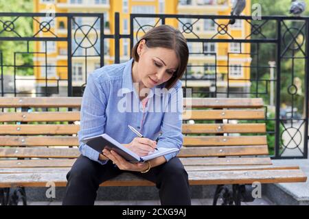 Reife seriöse Geschäftsfrau macht Notizen im Notizbuch Stockfoto