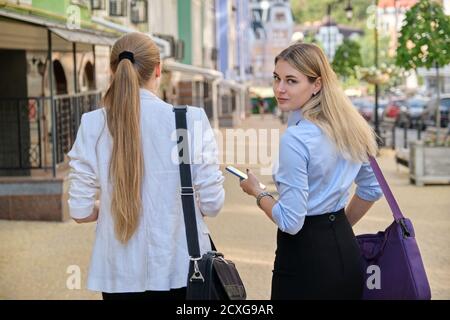 Rückaufnahme von zwei jungen Geschäftsfrauen beim Gehen und Sprechen In der Stadt Stockfoto