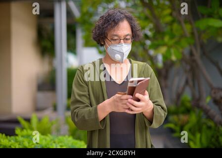 Japanischer Mann mit Maske mit Telefon im Dachgarten Stockfoto