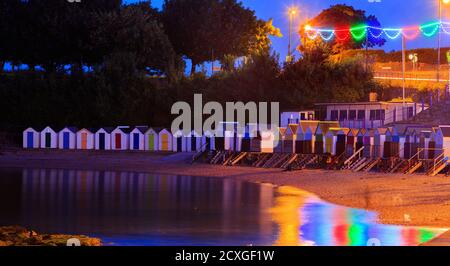 Meadfoot Beach - Torquay, 2017. Kleiner lokaler Strand mit bunten Strandhütten in der Abenddämmerung, mit Lichtern, die sich im ruhigen Meer spiegeln. Torquay ist ein beliebtes Meer Stockfoto