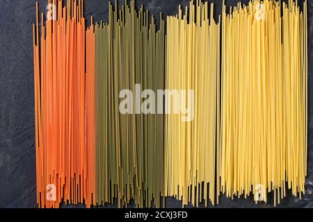 Trockene bunte Nudeln Spaghetti über schwarz strukturierten Hintergrund. Ansicht von oben Stockfoto