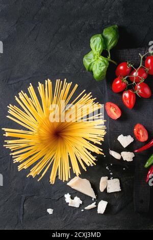 Zutaten für Pasta Sauce Tomaten, Basilikum, Knoblauch, Chili und Parmesan Käse mit trockenen Spaghetti auf Holz Schneidebrett über schwarz strukturiert Stockfoto