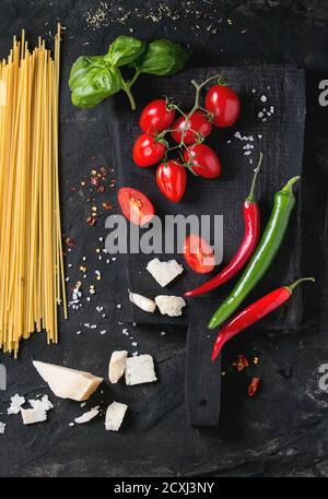 Zutaten für Pasta Sauce Tomaten, Basilikum, Knoblauch, Chili und Parmesan Käse mit trockenen Spaghetti auf Holz Schneidebrett über schwarz strukturiert Stockfoto