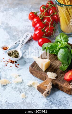 Zutaten für Pasta sauce Tomaten, Basilikum, Knoblauch, Paprika und Parmesan Käse mit trockenen Spaghetti auf Holz Schneidebrett über weiße strukturierte Stockfoto