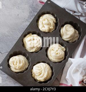 Bereiten Sie moderne Backwaren Cruffins, ganze und Scheiben, wie Croissant und Muffin. Teig in Silikonbackform auf weißem Küchentuch über grauem Rücken aufwirbeln Stockfoto