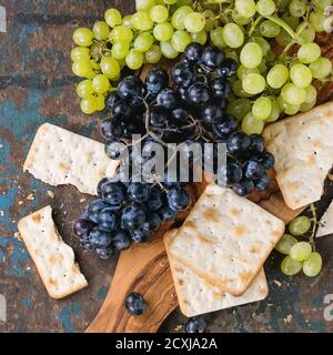 Trauben von reifen feuchten roten und weißen Trauben mit Crackern Snack auf Olivenholz Schneidebrett über alten dunklen Holzhintergrund. Draufsicht. Quadratisches Bild Stockfoto