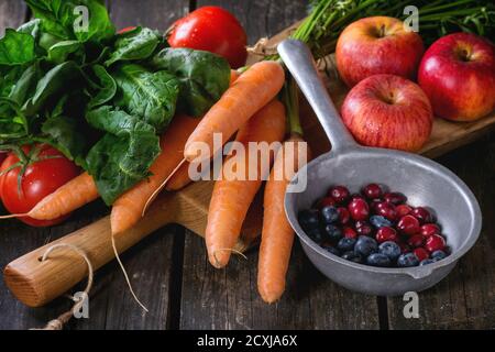 Auswahl von frischem Obst, Gemüse und Beeren. Bündel von Karotten, Spinat, Tomaten und rote Äpfel auf Schneidebrett, Blaubeeren und Preiselbeeren Stockfoto