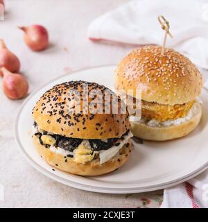 Zwei hausgemachte Veggie Burger mit Süßkartoffel und schwarzem Reis, serviert auf weißem Teller mit Küchentuch auf weißem strukturiertem Hintergrund. Quadratisches Bild Stockfoto
