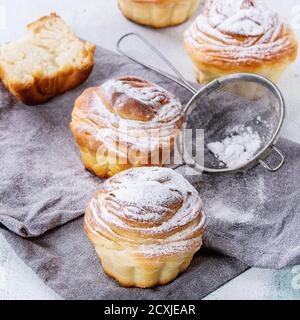 Moderne Backwaren Cruffins, ganz und in Scheiben, wie Croissant und Muffin mit Zuckerpulver, serviert auf grauer Textilserviette mit Vintage Sieb über weißem wo Stockfoto