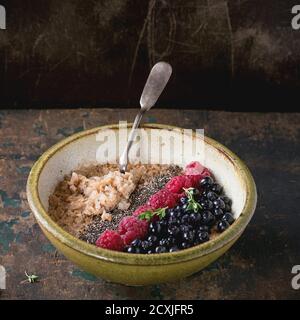 Schüssel Haferflocken Haferbrei mit Heidelbeeren, Himbeeren und Chia-Samen, serviert mit Vintage Löffel über alten Holz strukturierten Hintergrund. Rustikales Frühstück t Stockfoto