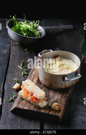 Vintage Aluminium Pfanne mit weißem Spargel Cremesuppe mit Erbse Sprossen, gesalzenen Lachs und Toast, auf Holz Schneidebrett über alte hölzerne backgr serviert. Stockfoto