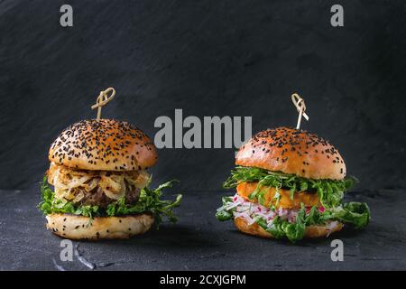 Hausgemachte traditionelle und vegetarische Burger mit Rindfleisch, gebratenen Zwiebeln, Süßkartoffeln, Rettich und Erbsensprossen, serviert auf schwarzem texturierten Hintergrund. Gesund V Stockfoto