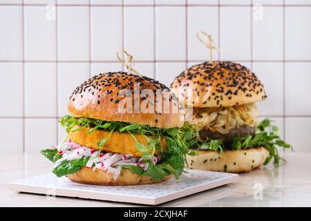 Hausgemachte traditionelle und vegetarische Burger mit Rindfleisch, gebratenen Zwiebeln, Süßkartoffeln, Rettich und Erbsensprossen, serviert auf weißem Marmor mit Fliesenboden. H Stockfoto