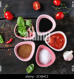 Zutaten für die Zubereitung von hausgemachter Tomatensoße. Tomaten, Salz, Zucker, Balsamico-Essig, Kräuter und Chilischoten in wenigen Keramikschüsseln über altem W Stockfoto