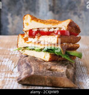 Kohlenhydratarme glutenfreie Cloud Bread Veggie Sandwich mit Spinat, Avocado, Feta-Käse, Tomaten und Pesto-Sauce, serviert auf Schneidebrett über Holztex Stockfoto