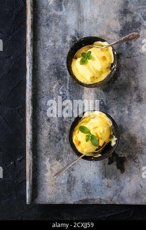 Hausgemachte Mango-Eis mit frischer Minze in Vintage Eisen Schalen über grau Metall strukturierten Hintergrund. Flach zu legen Stockfoto