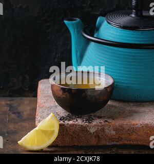 Keramik Tasse heißen schwarzen Tee mit Zitrone, serviert mit blauen Eisen Teekanne auf Ton Wildschwein über alten hölzernen Hintergrund. Quadratisches Bild Stockfoto