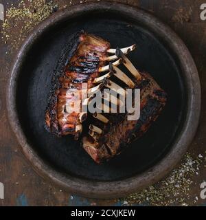 Ganze gegrillte lammkarree, serviert mit Gewürzen auf Lehm Tablett über alten Holzhintergrund. Overhead-Ansicht. Quadratisches Bild Stockfoto