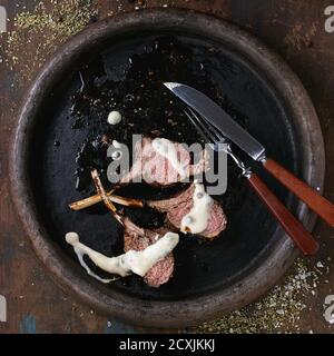 Gehackte gegrillte bbq-Lammkarree unter Pfeffersauce, serviert mit Gewürzen, Gabel und Messer auf Tonblech über alten Holzhintergrund. Draufsicht. Quadratisch Stockfoto