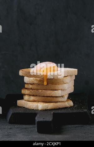 Stapel von Toastbrot mit Beginn fließenden gezuckerten gehärtetem Eigelb auf schwarzem Holz Schneidebrett über schwarzem texturierten Hintergrund. Stockfoto