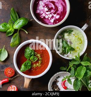 Auswahl an kalten vegetarischen Suppen Gazpacho Gurke mit Minze, Rote Beete mit Feta Chese, Tomaten mit grünem Pesto, serviert mit Gewürzen in Tassen über w Stockfoto