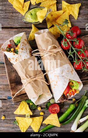 Mexikanisches Abendessen. Zwei tapeierte Tortillas Burrito mit Rindfleisch und Gemüse serviert mit Gemüse, Nachos Chips und Guacomole Sauce über alten Holz Stockfoto