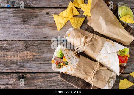 Mexikanisches Abendessen. Zwei tapeierte Tortillas mit Rindfleisch und Gemüse serviert mit Nachos-Chips und Guacomole-Sauce auf altem Holzhintergrund. Flach liegend Stockfoto