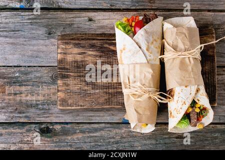 Mexikanisches Abendessen. Zwei tapeierte Tortillas Burrito mit Rindfleisch und Gemüse auf altem Holzhintergrund. Flach liegend. Mit Kopierbereich Stockfoto