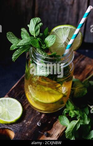 Ice grüner Tee mit Eis, frische Minze, Limette und Zitrone im Glas Marmeladenglas mit Retro cocktail Rohr, auf Holz Schneidebrett serviert mit alten hölzernen backgr Stockfoto