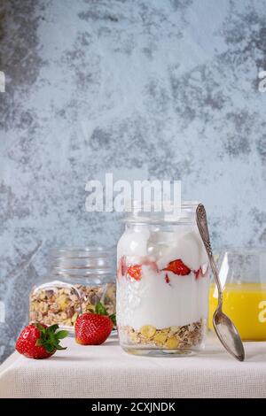 Gesundes Frühstück Müsli, Erdbeeren und Joghurt mit Mango Smoothie in Glas Maurergläser. Mit frischen Erdbeeren auf weißen Tischdecke mit textu serviert. Stockfoto