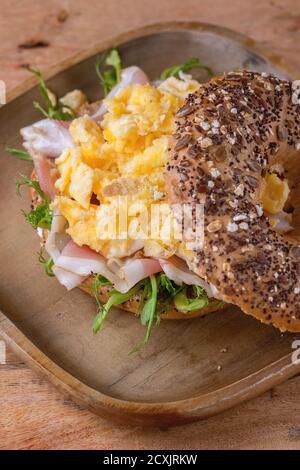 Geöffneten Vollkorn Brötchen mit Rührei, Erbse sprießen und Prosciutto-Schinken auf Holzplatte über hölzerne strukturierten Hintergrund. Stockfoto