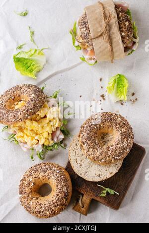 Leer und mit Vollkorn-Bagels mit Rührei, Erbsensprossen, gebratenen Zwiebeln und Schinken, auf weißen Leinentischdecken und kleinen Holztäfelchen zubereitet Stockfoto