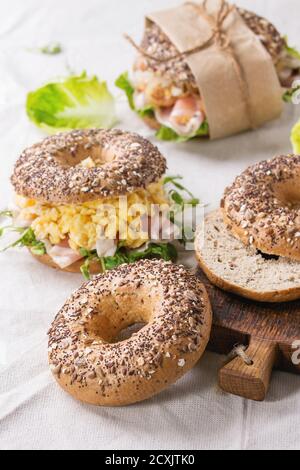 Leer und mit Vollkorn-Bagels mit Rührei, Erbsensprossen, gebratenen Zwiebeln und Schinken, auf weißen Leinentischdecken und kleinen Holztäfelchen zubereitet Stockfoto