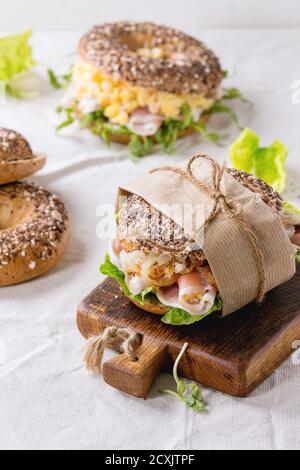 Leer und Personal streuen Samen Vollkorn Bagels mit Rührei, Erbsensprossen, gebratene Zwiebeln und Schinken, so dass auf weißen Leinentischtuch A Stockfoto