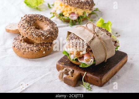 Leer und Personal streuen Samen Vollkorn Bagels mit Rührei, Erbsensprossen, gebratene Zwiebeln und Schinken, so dass auf weißen Leinentischtuch A Stockfoto