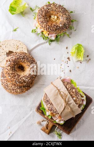 Leer und mit Vollkorn-Bagels mit Rührei, Erbsensprossen, gebratenen Zwiebeln und Schinken, auf weißen Leinentischdecken und kleinen Holztäfelchen zubereitet Stockfoto