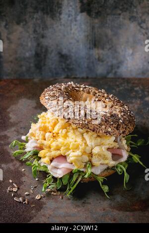 Geöffneten Vollkorn Brötchen mit Rührei, Erbse sprießen und Prosciutto-Schinken über alten rostigen Eisen strukturierten Hintergrund. Stockfoto