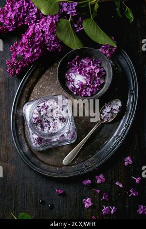 Anordnung mit Vintage Iron Bowl und Glas Glas lila Blumen in Zucker, silbernen Löffel und Flieder Zweig auf Vintage Tablett über schwarzen Holz Hintergrund Stockfoto