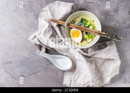 Weiße Schale mit asiatischen Stil Suppe mit Rührei, die Hälfte der marinierte Ei, Frühlingszwiebeln, Spinat serviert mit hölzernen Stäbchen, Löffel, Textile über gra Stockfoto