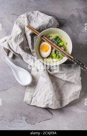 Weiße Schale mit asiatischen Stil Suppe mit Rührei, die Hälfte der marinierte Ei, Frühlingszwiebeln, Spinat serviert mit hölzernen Stäbchen, Löffel, Textile über gra Stockfoto