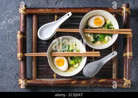Zwei Schalen mit asiatischen Stil Suppe mit Rührei, die Hälfte der marinierte Ei, Frühlingszwiebeln, Spinat serviert mit hölzernen Stäbchen und Löffel auf Bambus tra Stockfoto
