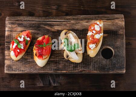 Verschiedene Mini-Bruschetta mit Tomaten, Erdbeeren, Feta-Käse, Huhn, Pilze und Basilikum auf getoastetem Baguette, serviert auf Holz Schneidebrett o Stockfoto