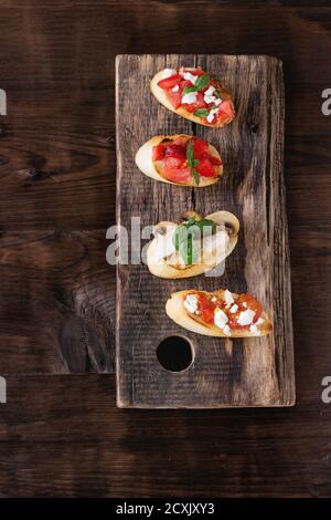 Verschiedene Mini-Bruschetta mit Tomaten, Erdbeeren, Feta-Käse, Huhn, Pilze und Basilikum auf getoastetem Baguette, serviert auf Holz Schneidebrett o Stockfoto