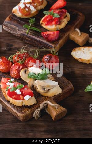 Verschiedene Mini-Bruschetta mit Tomaten, Erdbeeren, Feta-Käse, Huhn, Pilze und Basilikum auf getoastetem Baguette, serviert auf Holz Schneidebrett o Stockfoto